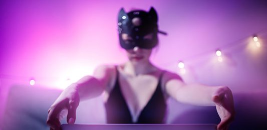 Internet Webcam Model in BDSM Katzenmaske sitzt vor Laptop