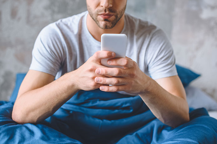 Mann mit Smartphone im Bett